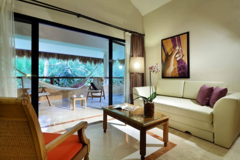 Salón con sofá y ventanal al jardín de una suite del Grand Palladium Riviera Maya