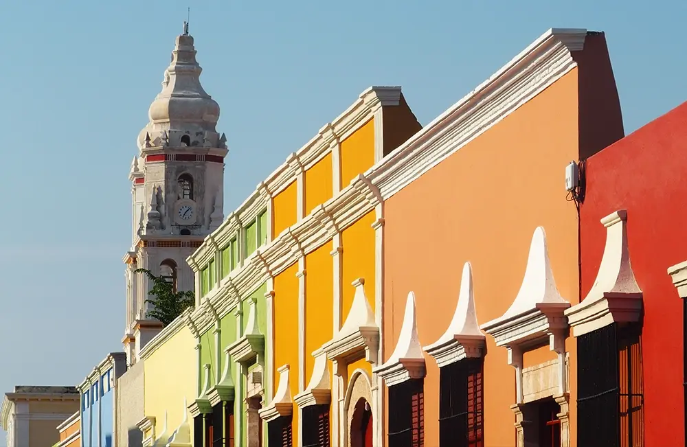 Calle de casas coloniales de colores con la torre de una iglesia al fondo
